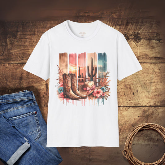 White t-shirt with a cowboy boot and cactus design on a wooden surface with jeans and rope.