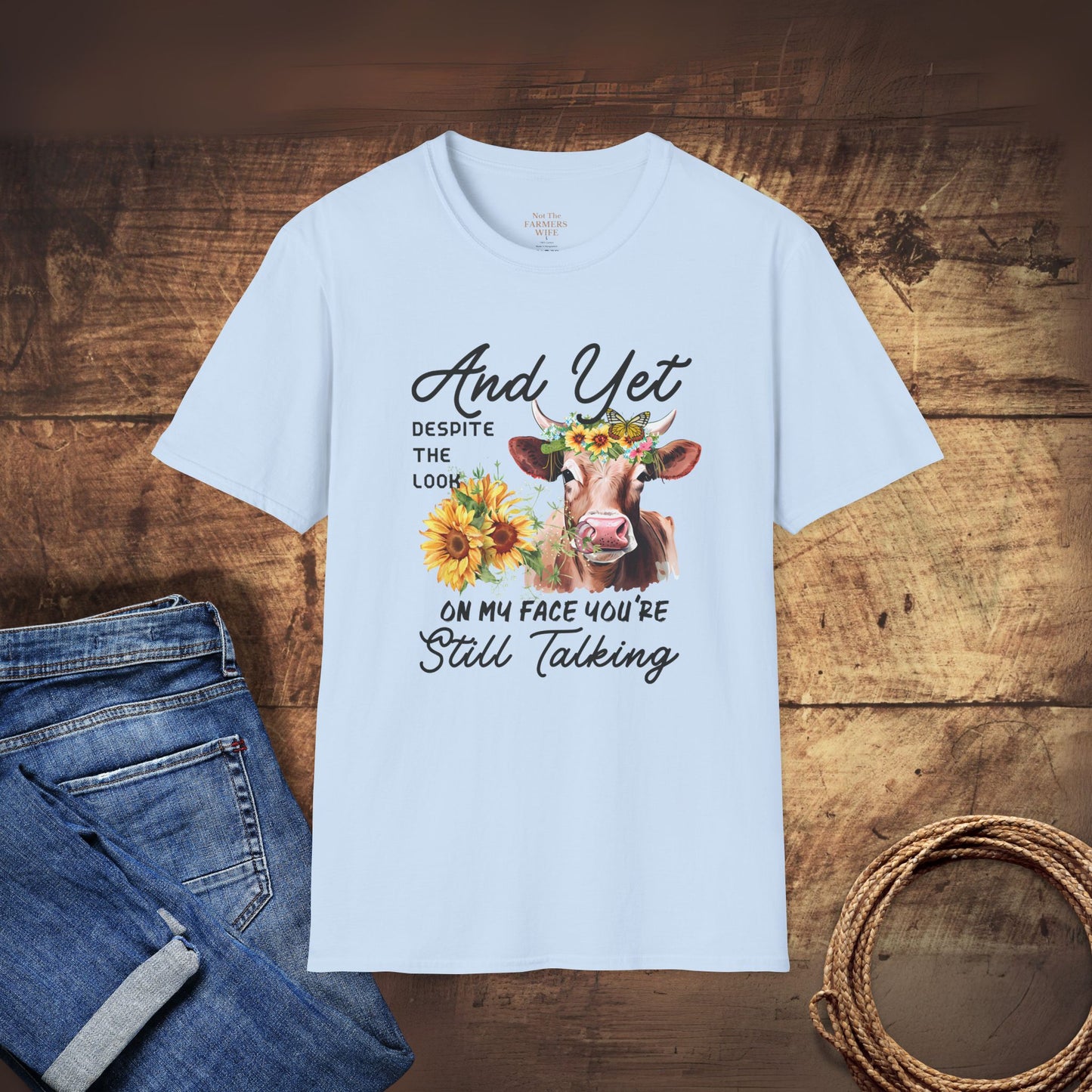 Light blue t-shirt with a cow graphic and text on a wooden surface with jeans and rope.