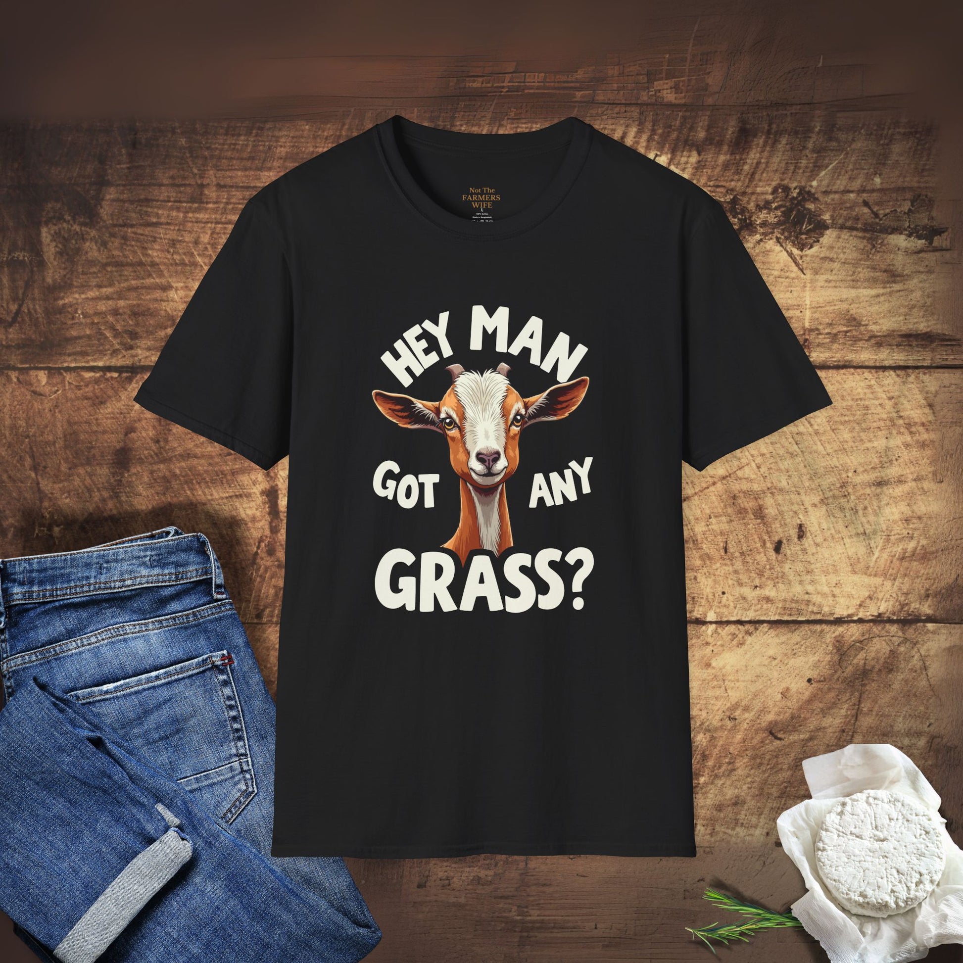 Black t-shirt with a goat graphic and text on a wooden surface with jeans and hay.